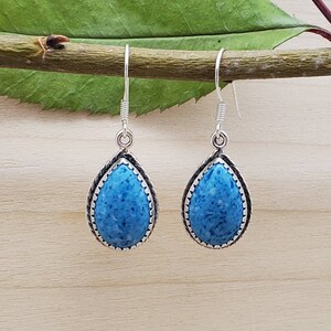 May include: A pair of silver dangle earrings with a teardrop-shaped blue stone set in a silver bezel. The stone has a speckled pattern.