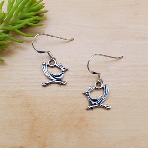 May include: A pair of silver earrings featuring a stylized roadrunner design. The earrings are dangle style with a hook closure.