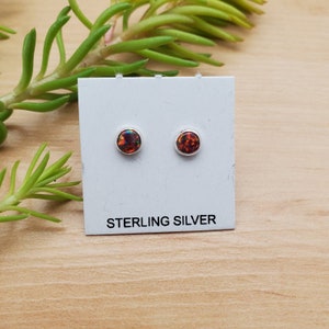 Może przedstawiać: Para srebrnych kolczyków z małymi, okrągłymi, opalizującymi kamieniami opalu. Kolczyki są prezentowane na białej kartce z napisem "STERLING SILVER".