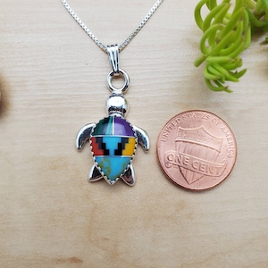 Peut inclure: Pendentif en argent sterling en forme de tortue avec une incrustation colorée de turquoise, rouge, jaune, noir, violet et vert. Le pendentif est à peu près de la taille d'une pièce de monnaie française.