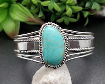May include: A silver cuff bracelet with a turquoise stone set in a rope design. The bracelet has three bands with a rope design and a smooth silver band.
