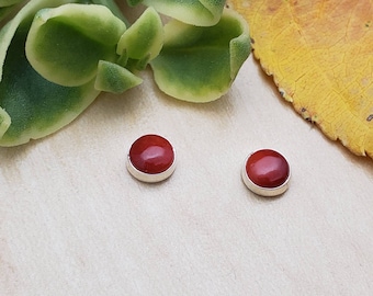 May include: A pair of red gemstone stud earrings with silver settings. The earrings are small and round.