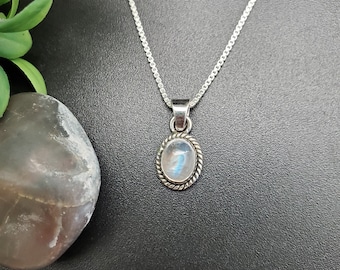 May include: A silver chain necklace with a silver oval pendant featuring a moonstone gemstone.