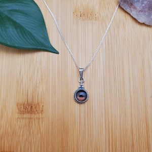 Pu&ograve; includere: Una collana con catena d'argento con un ciondolo rotondo che presenta una pietra preziosa marrone scuro incastonata in una ghiera d'argento.