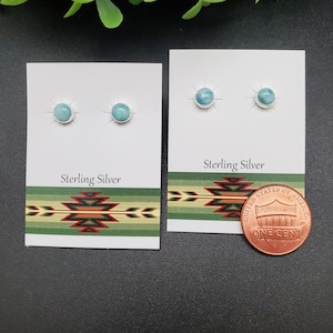 May include: Two pairs of sterling silver earrings with turquoise stones on white cards with a Southwestern design. The cards also say "Sterling Silver". A penny is included for size reference.