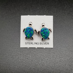 May include: Sterling silver earrings featuring a green and blue opal turtle design. The earrings are on a white card with the words "Sterling Silver" printed on it.