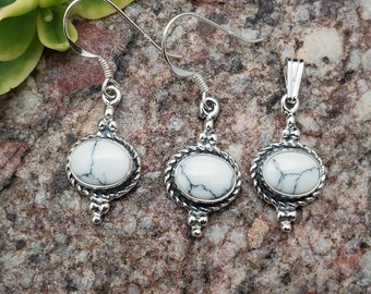 May include: A set of silver earrings and a pendant featuring white oval-shaped stones with a marbled pattern. The stones are set in a silver frame with a rope-like design and a beaded detail.