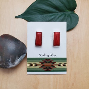 Puede incluir: Un par de pendientes de plata de ley con piedras rectangulares de coral rojo. Los pendientes se muestran en una tarjeta blanca con el texto "Sterling Silver".