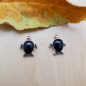 May include: A pair of silver turtle earrings with black onyx stones. The earrings are small and delicate.