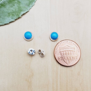 May include: A pair of sterling silver earrings with turquoise stones. The earrings are shown next to a US penny for size comparison.