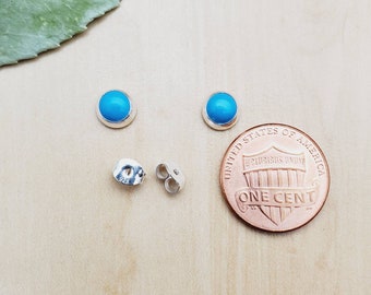 May include: A pair of sterling silver earrings with turquoise stones. The earrings are shown next to a UK penny for size comparison.