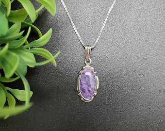 May include: A silver chain necklace with a purple oval pendant. The pendant has a detailed silver frame and a purple stone with a swirling pattern.