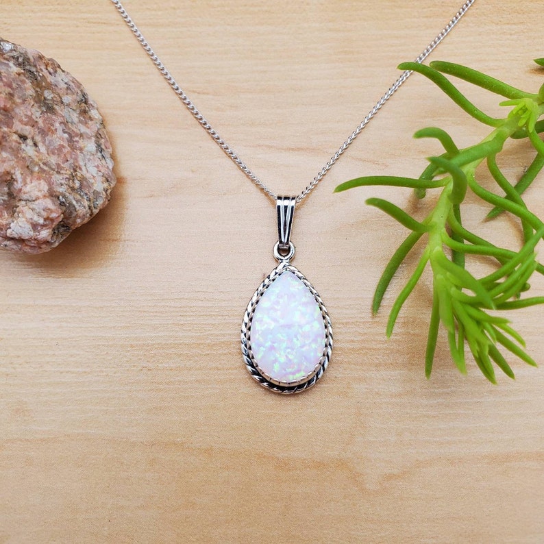 May include: A silver chain necklace with a teardrop-shaped pendant featuring a white opal stone with a silver border.
