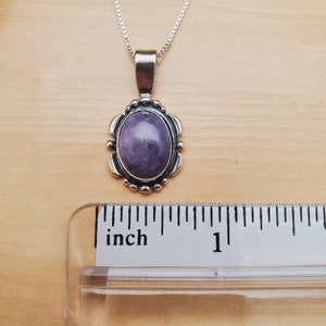 May include: A silver pendant with a purple amethyst stone set in a silver oval frame. The pendant is about 1 inch long.