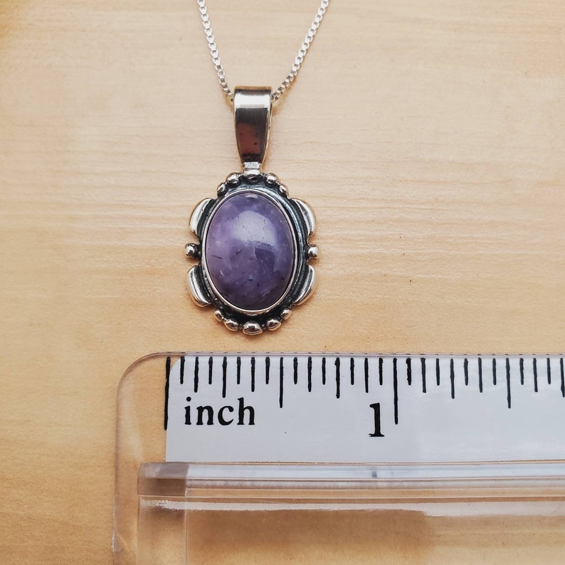 May include: A silver pendant with a purple amethyst stone set in a silver oval frame. The pendant is about 1 inch long.