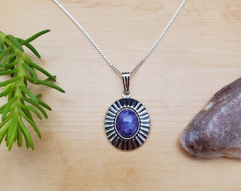 Peut inclure: Un collier en chaîne argent avec un pendentif en pierre précieuse violette. Le pendentif est de forme ovale et présente un motif de soleil argenté autour de la pierre.