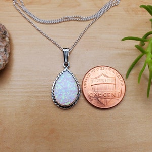 May include: A silver chain necklace with a teardrop-shaped opal pendant set in a silver bezel. The pendant is about the size of a US penny.