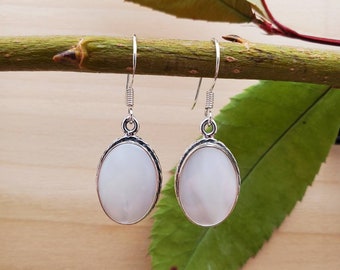 May include: A pair of silver earrings with oval-shaped white mother of pearl stones.