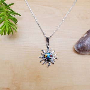 May include: A silver necklace with a sun pendant featuring a colorful inlay of turquoise, red, yellow, and black stones.