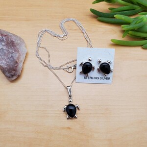 May include: A sterling silver necklace and earrings set featuring black onyx turtle pendants. The set comes on a silver chain and includes a card that reads "Sterling Silver".