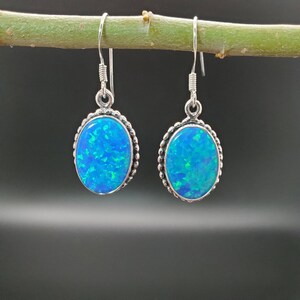 May include: A pair of silver dangle earrings with oval blue opal gemstones. The earrings have a beaded border around the gemstones.