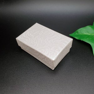 May include: A white cardboard box with a textured, wavy pattern. The box is closed and sitting on a black surface.