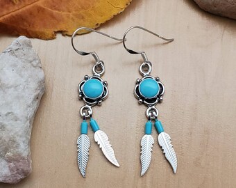 May include: A pair of silver dangle earrings with turquoise stones and silver feathers. The earrings have a simple design and are perfect for everyday wear.