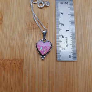 May include: A silver heart-shaped pendant necklace with a pink opal stone. The pendant is approximately 1 inch in size.