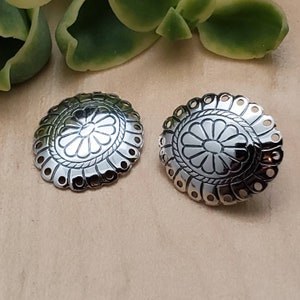 May include: A pair of silver earrings with a floral design. The earrings are round and have a scalloped edge.