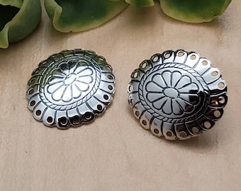 May include: A pair of silver earrings with a floral design. The earrings are round and have a scalloped edge.