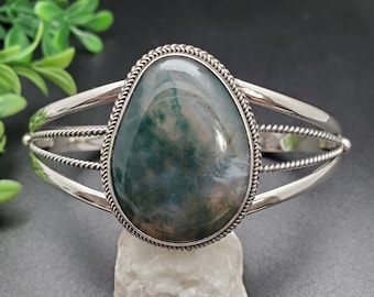May include: A silver bracelet featuring a green and white agate stone set in a silver bezel. The bracelet has a rope-like design on the band.