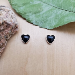 May include: A pair of silver heart-shaped stud earrings with black onyx stones.