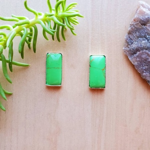 May include: A pair of green gemstone earrings with silver settings. The earrings are rectangular in shape and have a smooth, polished finish.