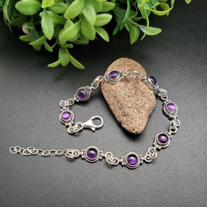 May include: A silver bracelet with a chain link design and six round purple amethyst gemstones.