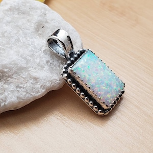 May include: A silver pendant with a white opal gemstone set in a beaded border.