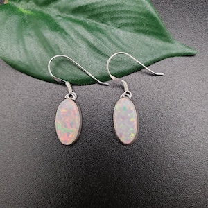 May include: A pair of silver dangle earrings with oval-shaped opal stones. The opals have a white base with iridescent rainbow colors.