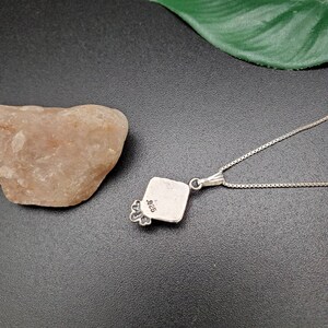 May include: Silver pendant necklace with a square pendant featuring a floral design. The back of the pendant is stamped with "925".