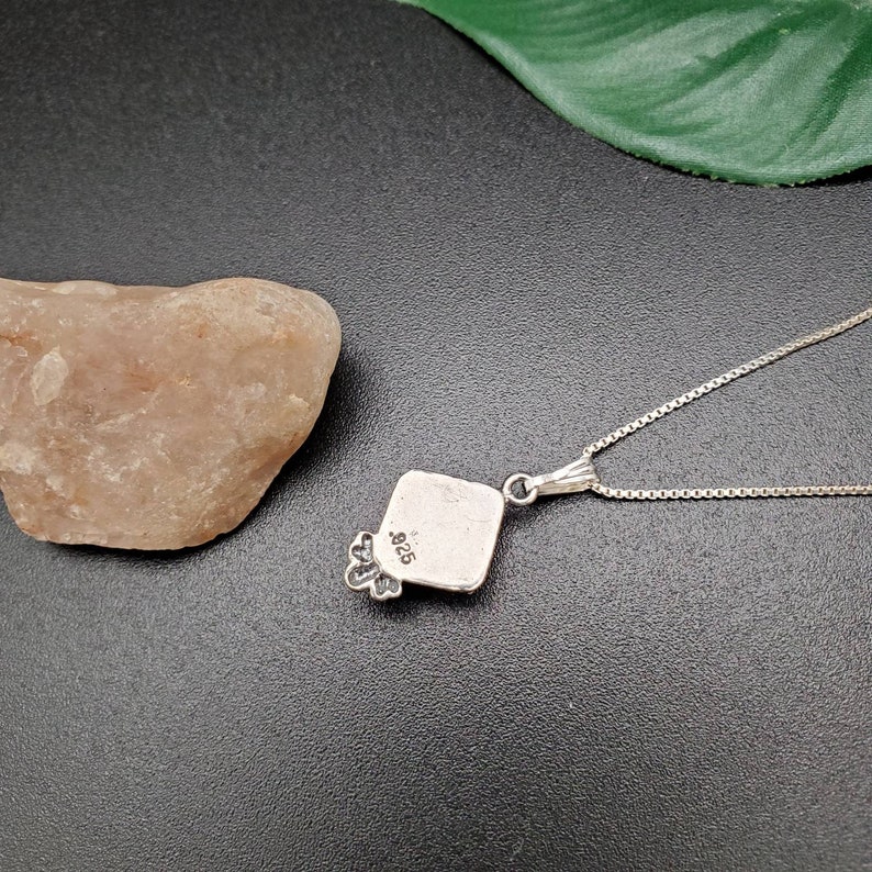 May include: Silver pendant necklace with a square pendant featuring a floral design. The back of the pendant is stamped with "925".