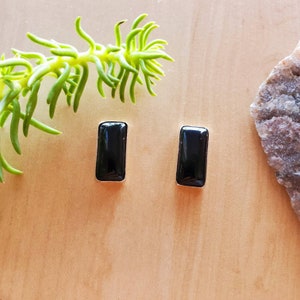 May include: A pair of black onyx earrings with silver settings. The earrings are rectangular in shape and have a polished finish.