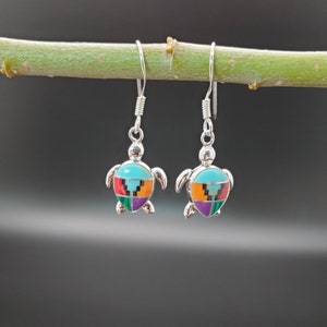 May include: A pair of silver dangle earrings featuring a turquoise, orange, red, green, and purple inlay turtle design.