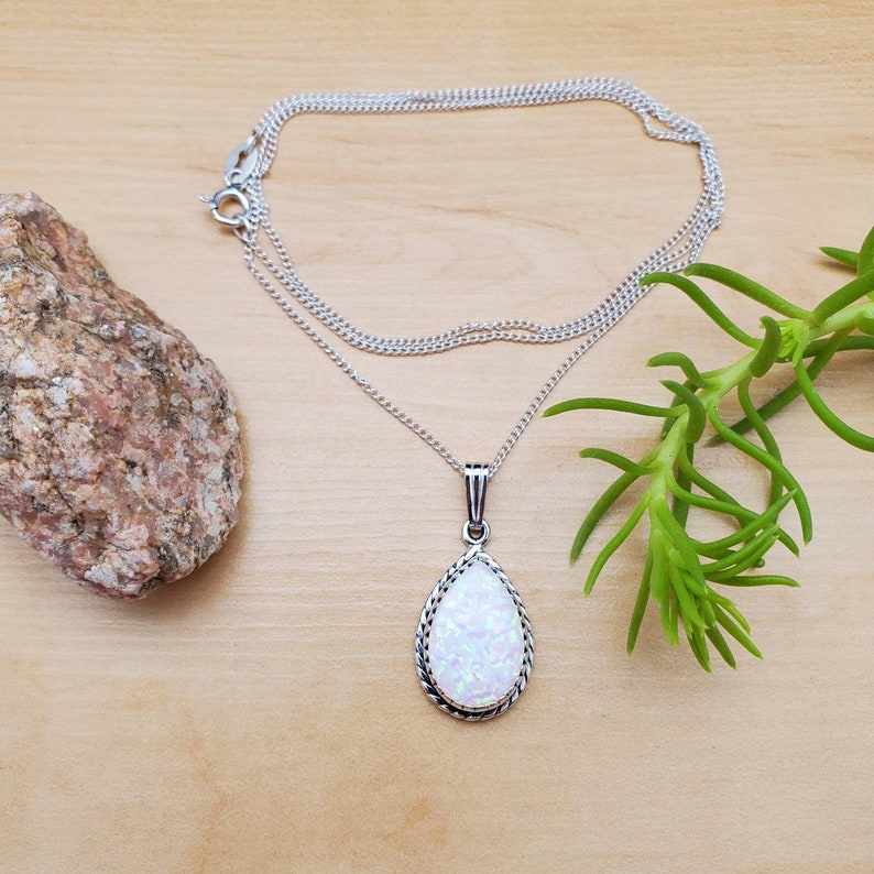 May include: A silver chain necklace with a teardrop-shaped pendant featuring a white opal stone.