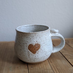 Puede incluir: Taza de cerámica blanca con motas marrones y un diseño de corazón marrón.