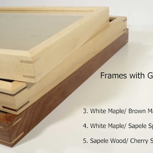 Peut inclure: Trois cadres photo en bois avec verre, empilés les uns sur les autres. Le cadre supérieur est en érable blanc avec des chevilles en érable brun. Le cadre du milieu est en érable blanc avec des chevilles en sapelli. Le cadre inférieur est en bois de sapelli avec des chevilles en cerisier. Le texte "Cadres avec verre" est visible sous les cadres.