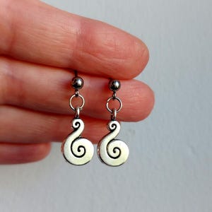May include: A pair of silver-toned drop earrings featuring a small metal ball stud connected to a dangling spiral charm. The earrings have a polished finish and a simple, symmetrical design, with each spiral charm hanging from a small circular jump ring.
