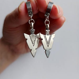 May include: A pair of silver arrowhead earrings. Each earring has a V-shaped design with a textured centre and a hinged clasp. The earrings are suspended from a small chain.