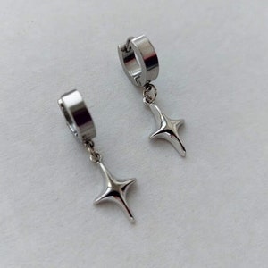 May include: A pair of silver hoop earrings with a star-shaped dangle charm. The earrings are made of stainless steel and have a polished finish.