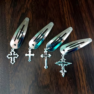 Könnte beinhalten: Vier silberne Haarklammern mit Kreuzanhängern. Die Kreuze sind in verschiedenen Stilen und Größen.