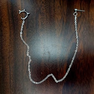 May include: A silver chain earring with a small, pointed crescent moon charm at the top.