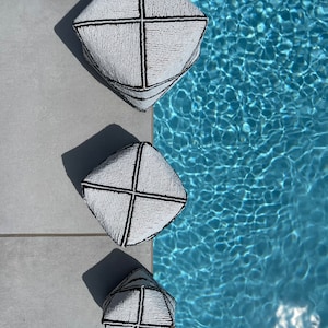 Puede incluir: Tres cestas de cuentas blancas y negras de diferentes tamaños, dispuestas en una pila vertical, con la cesta más grande en la parte superior. Las cestas están sobre una superficie de baldosas grises junto a una piscina azul.