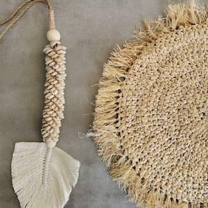 May include: A natural fiber placemat with a fringe border and a white feather tassel hanging from a string of wooden beads.